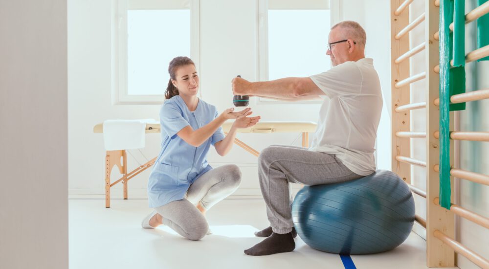 Young professional physiotherapist exercising with an injured patient using a blue ball Young professional physiotherapist exercising with an injured patient using a blue ball