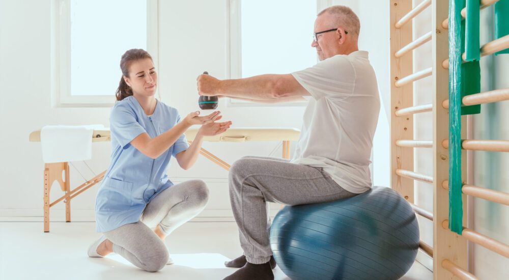 Young professional physiotherapist exercising with an injured patient using a blue ball