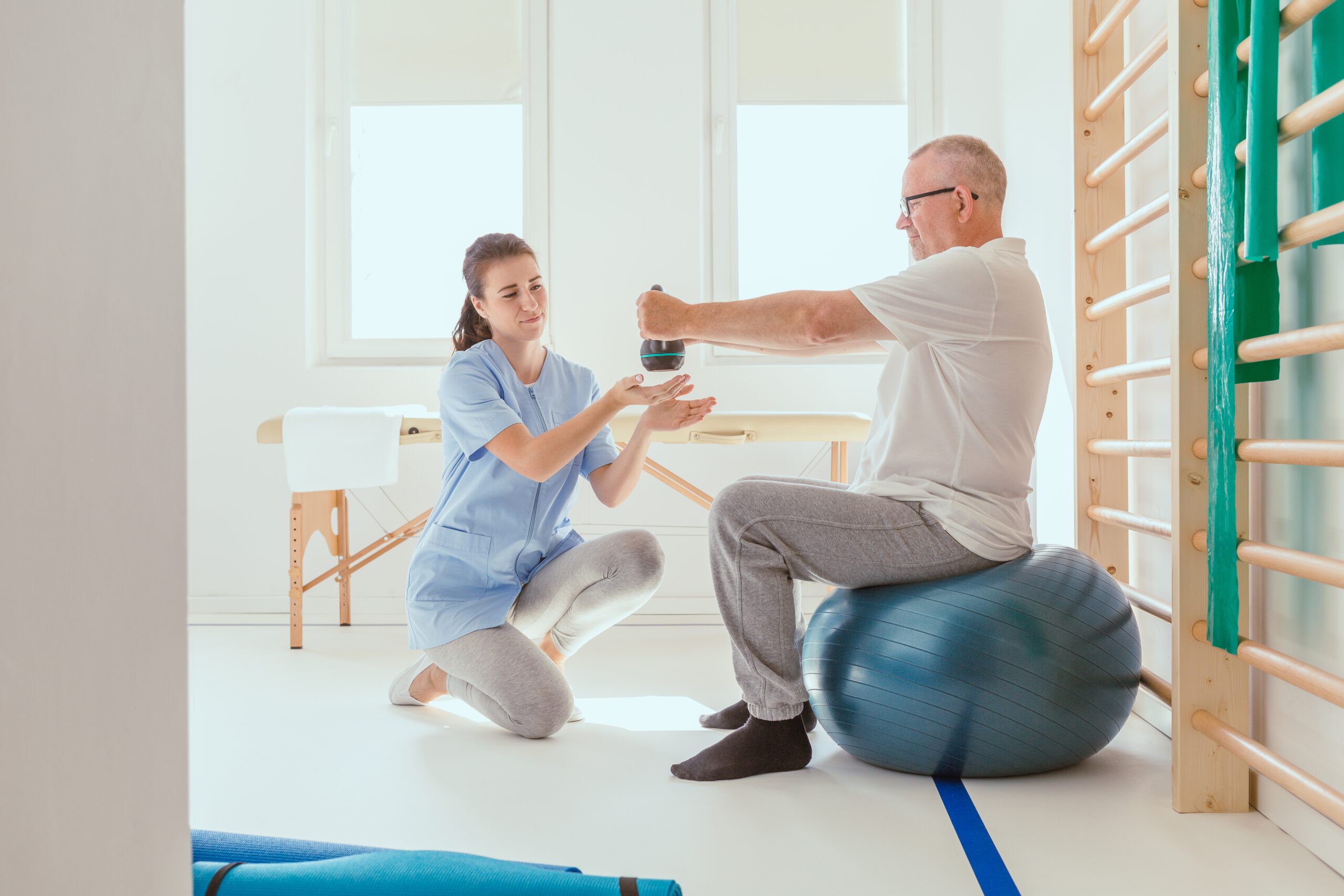 Young professional physiotherapist exercising with an injured patient using a blue ball