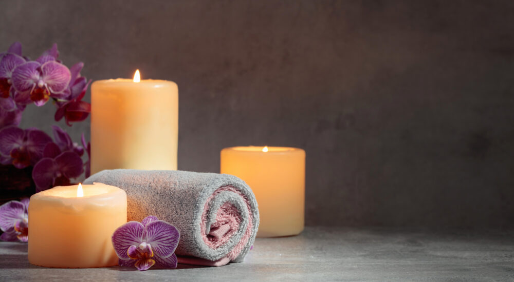 Towels, orchid flowers, and burning candles on a grey background. Spa concept with copy space.