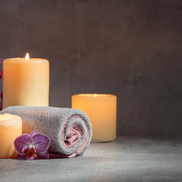 Towels, orchid flowers, and burning candles on a grey background. Spa concept with copy space.